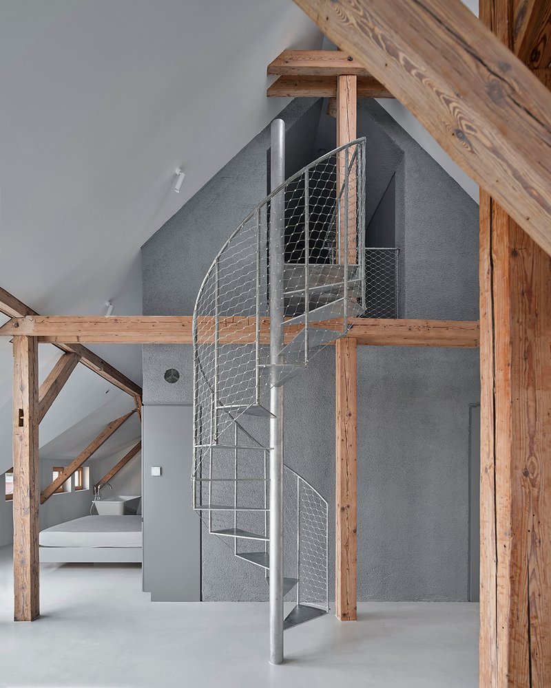 Close-up of wire mesh spiral staircase against charcoal wall plane within timber-framed attic space