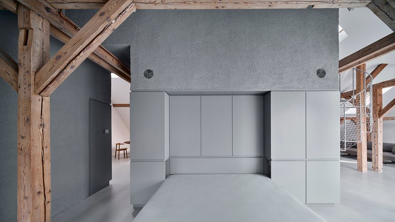 Grey kitchenette volume with flush cabinet panels and concrete countertop surrounded by exposed timber framing