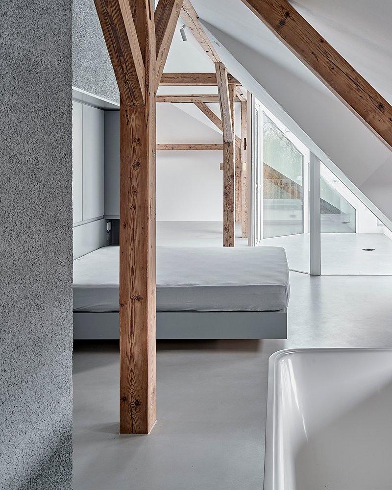 Sleeping area with bed positioned between timber columns beneath sloped ceiling with skylights