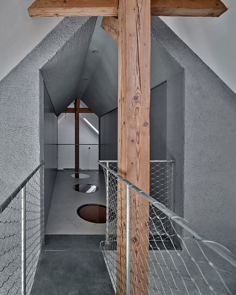 Upper level walkway with wire mesh railing and circular floor openings beside timber post