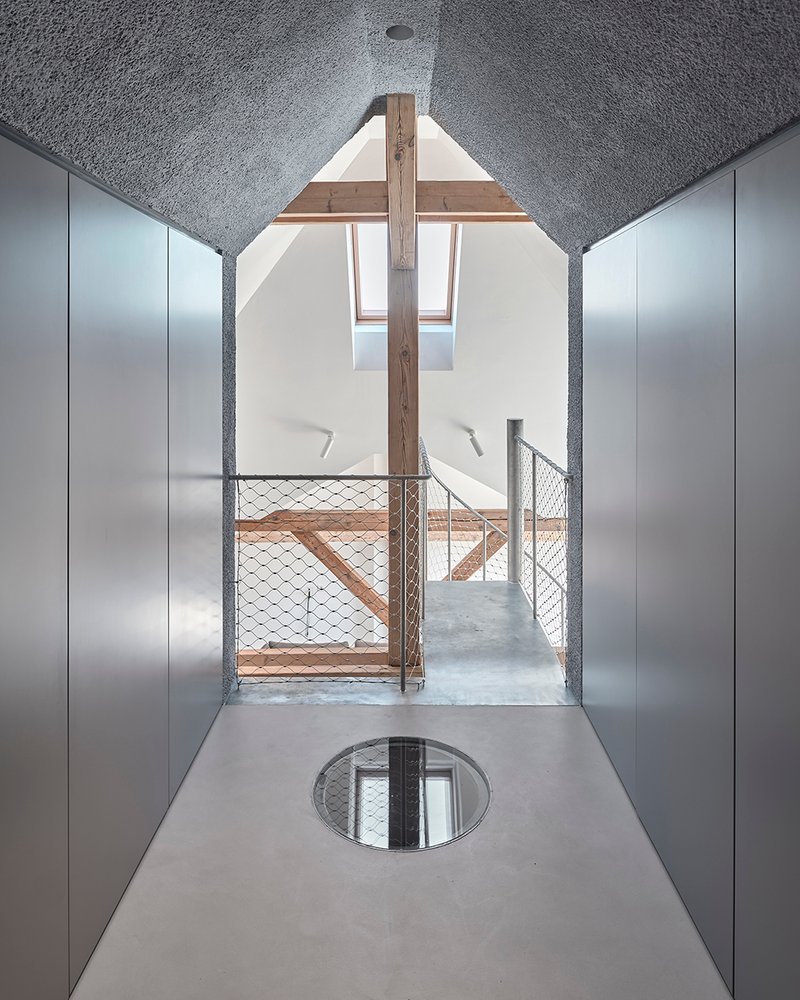 Attic corridor with circular skylight in the polished floor and exposed timber beams under textured ceiling