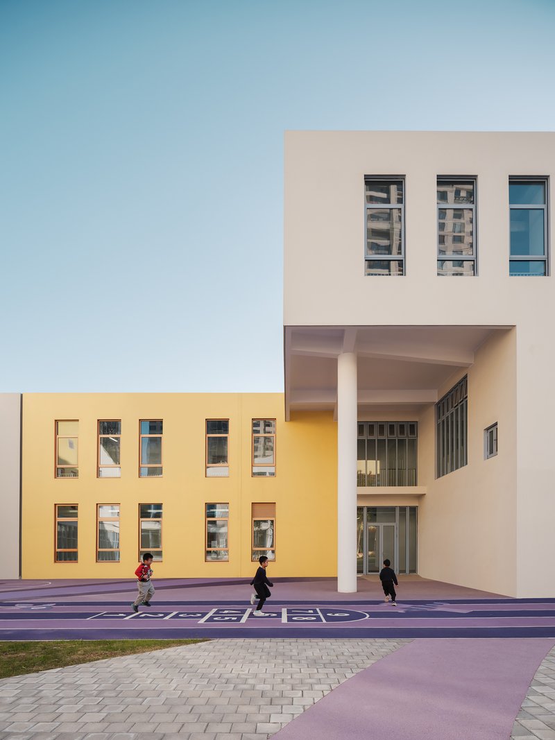 Courtyard view showing yellow and beige facades with a covered entry and children playing on purple pavement