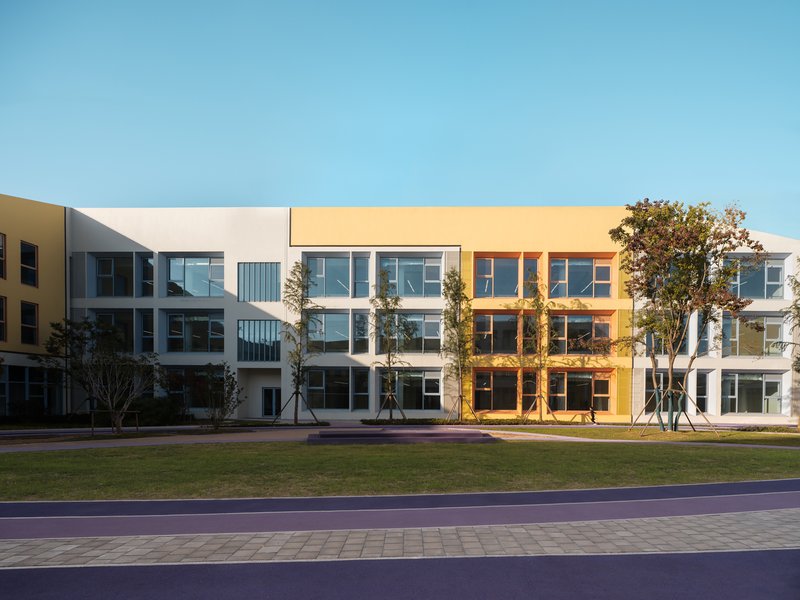 Courtyard facade showing alternating yellow and white volumes with young trees planted along the purple pathway