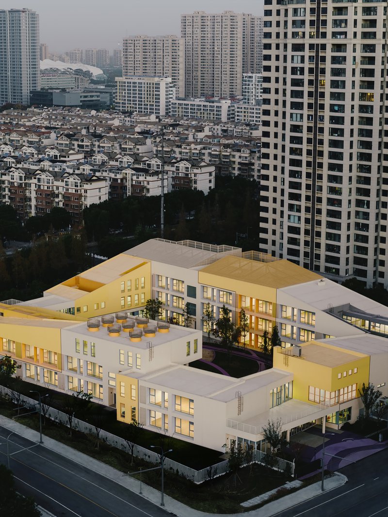 Aerial view of the white terraced school building with interior courtyard surrounded by high-rise towers at dusk