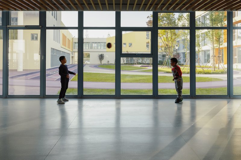 Interior corridor with floor-to-ceiling glazing and two children playing with a ball