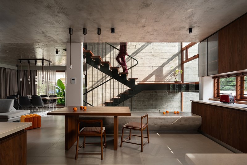 Open living and dining space with steel staircase beneath board-formed concrete ceiling and walls