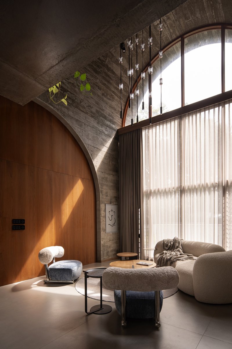 Curved timber wall beneath arched concrete vault with sheer curtains filtering daylight from tall windows