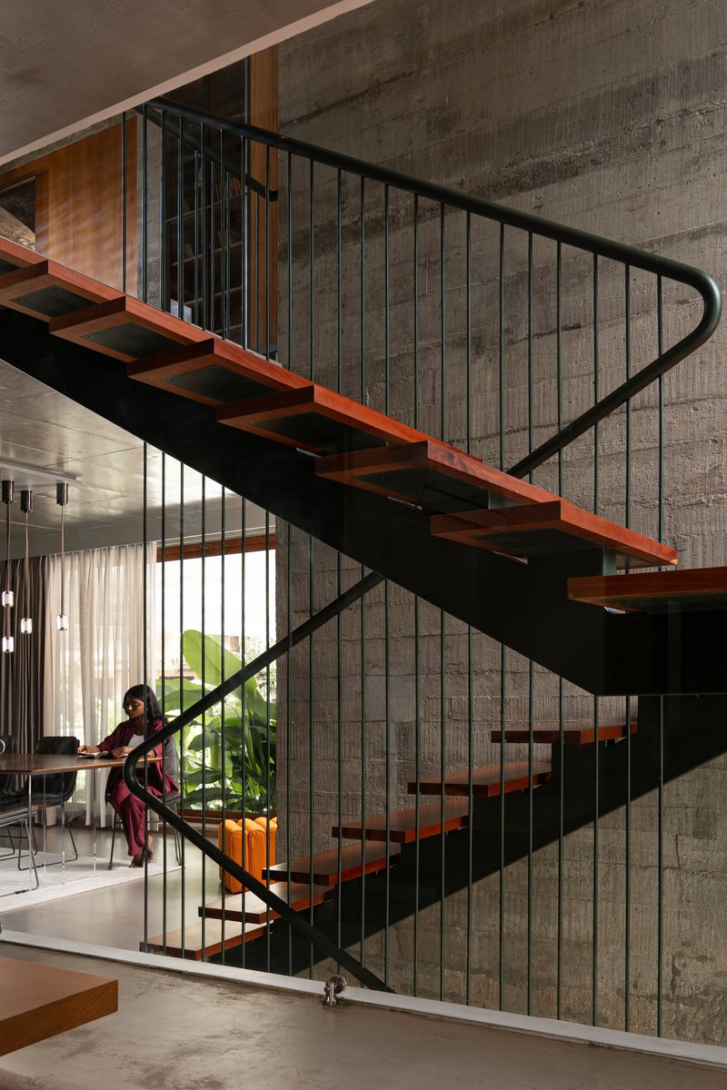 Timber and steel staircase with vertical rod balustrade against board-formed concrete wall as a person ascends