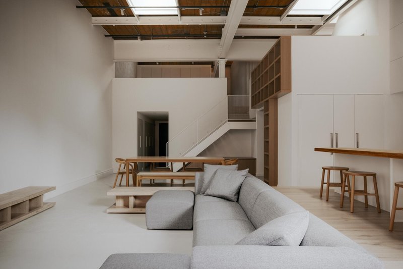 Double-height living space with exposed timber ceiling joists and skylights above a mezzanine with open shelving