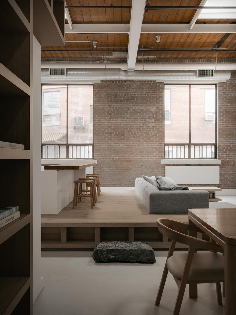 Raised platform living area with exposed brick wall and large industrial windows framing an adjacent building