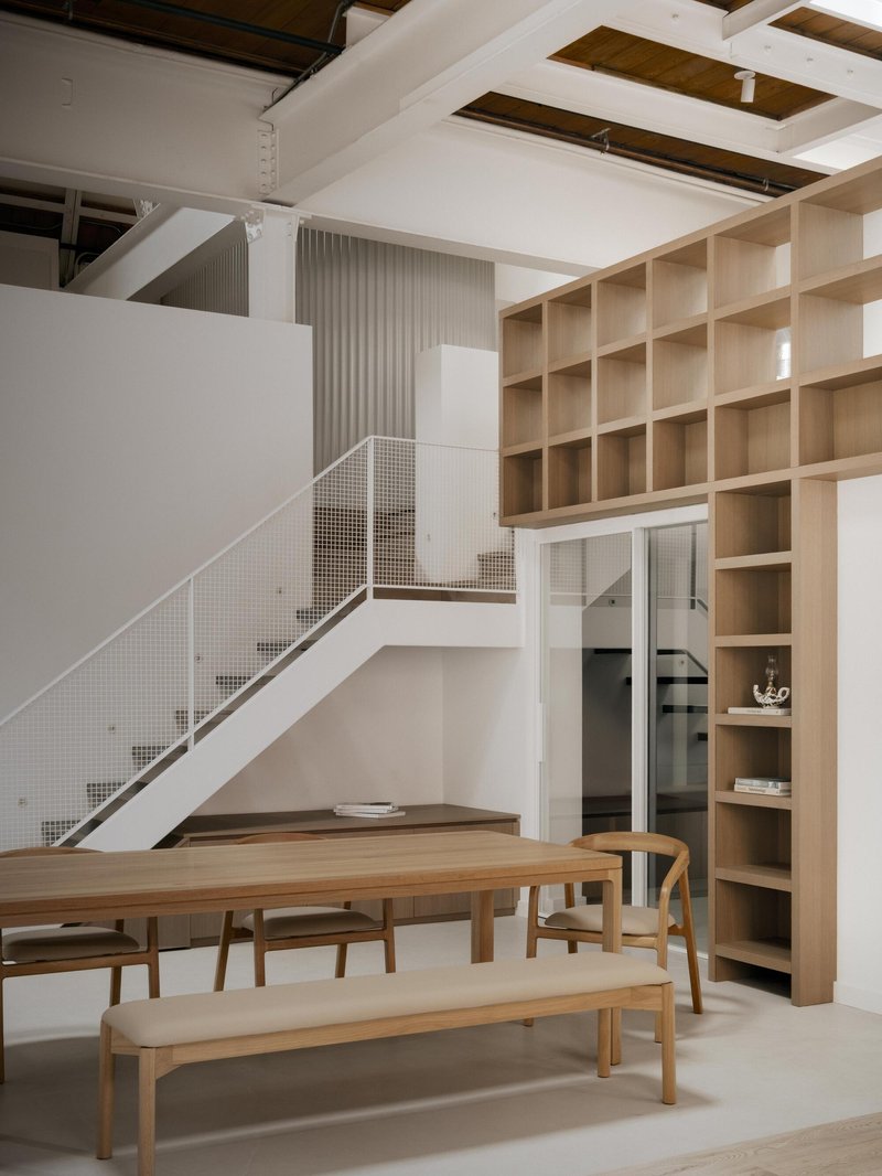 View of the white staircase with perforated metal balustrade beneath a floor-to-ceiling timber shelving wall