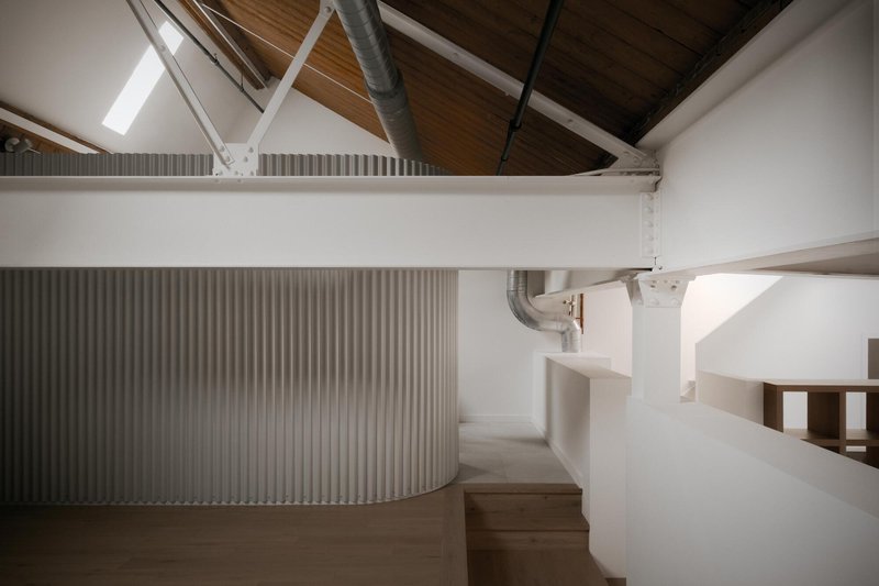 Curved staircase with corrugated metal cladding rising beneath a pitched timber ceiling with exposed ductwork