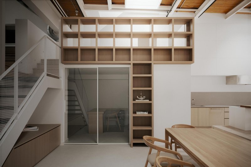 Timber shelving unit spanning from floor to exposed ceiling grid beside sliding glass doors