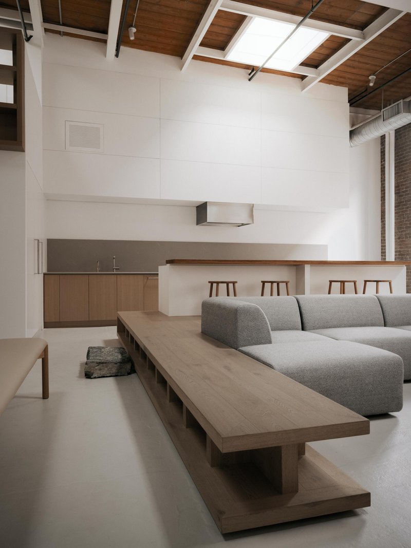 Open-plan living space with timber kitchen counter and grey sectional sofa under exposed wood-beam ceiling