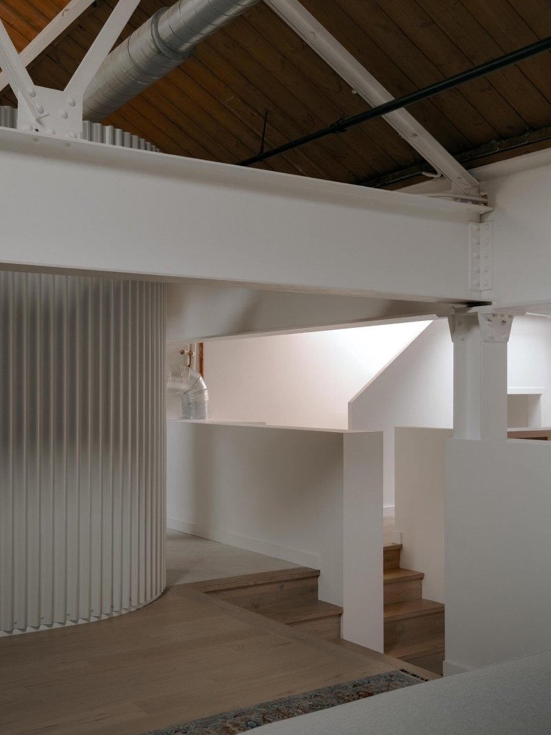 Timber staircase with white wall wrapping around curved vertical louver screen under exposed wood ceiling