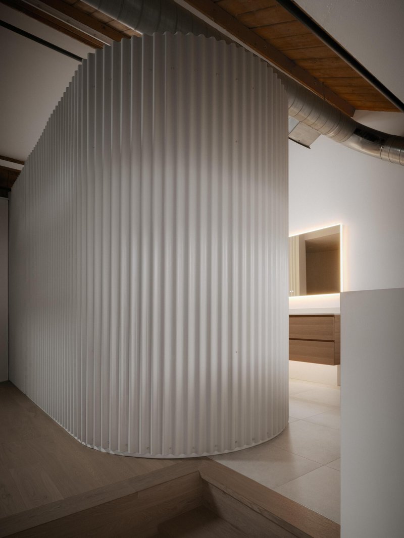 Curved white louver screen enclosing volume with glimpse of backlit timber cabinetry beyond