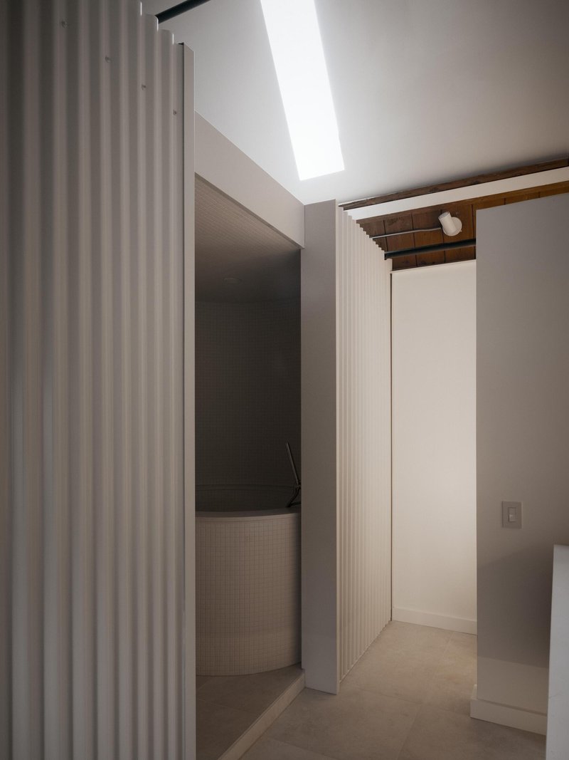 Interior hallway with fluted wall panels and a linear skylight casting daylight onto white surfaces