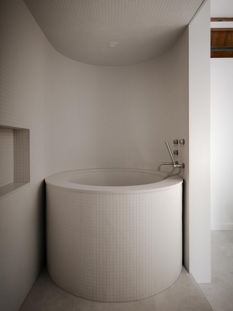 Cylindrical mosaic tile bathtub nestled in an alcove with curved walls and overhead light fixture