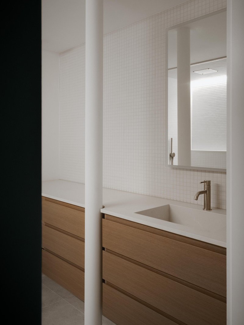 Bathroom vanity with oak drawer fronts and integrated sink viewed through a dark doorway