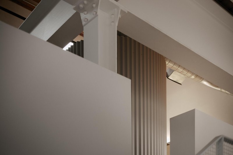 Interior view of white steel beams with bolted connections and fluted wall panel under ambient lighting