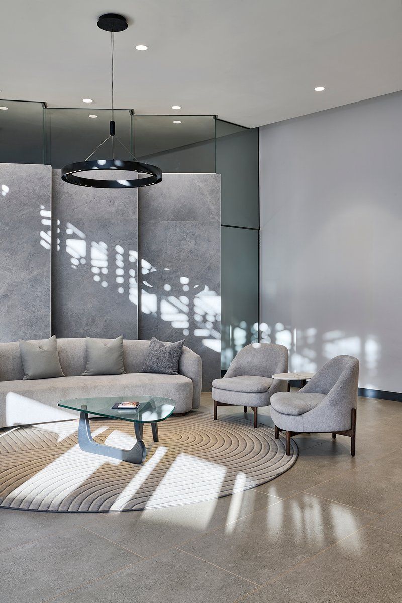 Double-height lounge with filtered light casting geometric shadows across concrete panels and polished floor