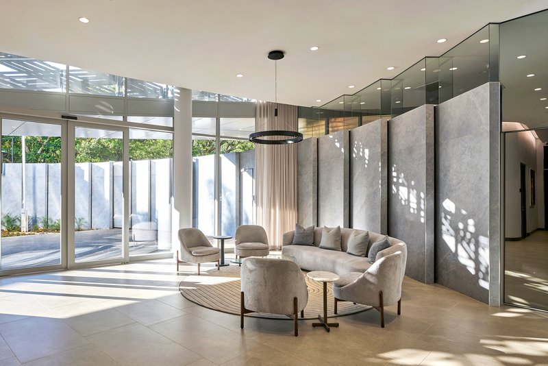 Interior seating area with floor-to-ceiling glazing overlooking courtyard and patterned light on concrete walls