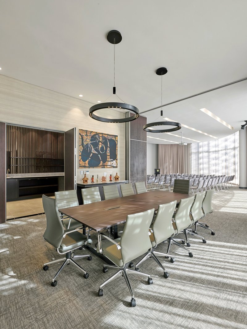 Conference room with long wooden table and white leather chairs beneath black circular pendant lights