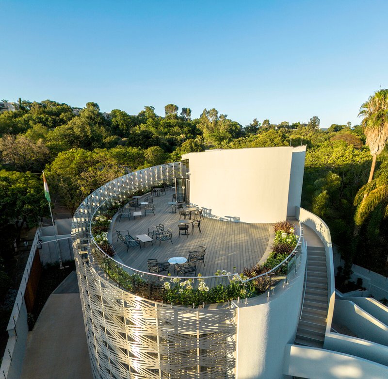 Aerial view of curved rooftop terrace with outdoor furniture and planted beds in late afternoon light
