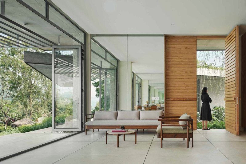 Open living space with folding glass walls, timber feature wall, and a figure standing by the courtyard