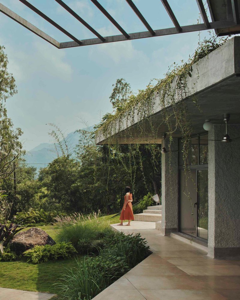 Covered walkway with concrete pergola beams and planted roof edges framing a view toward distant mountains