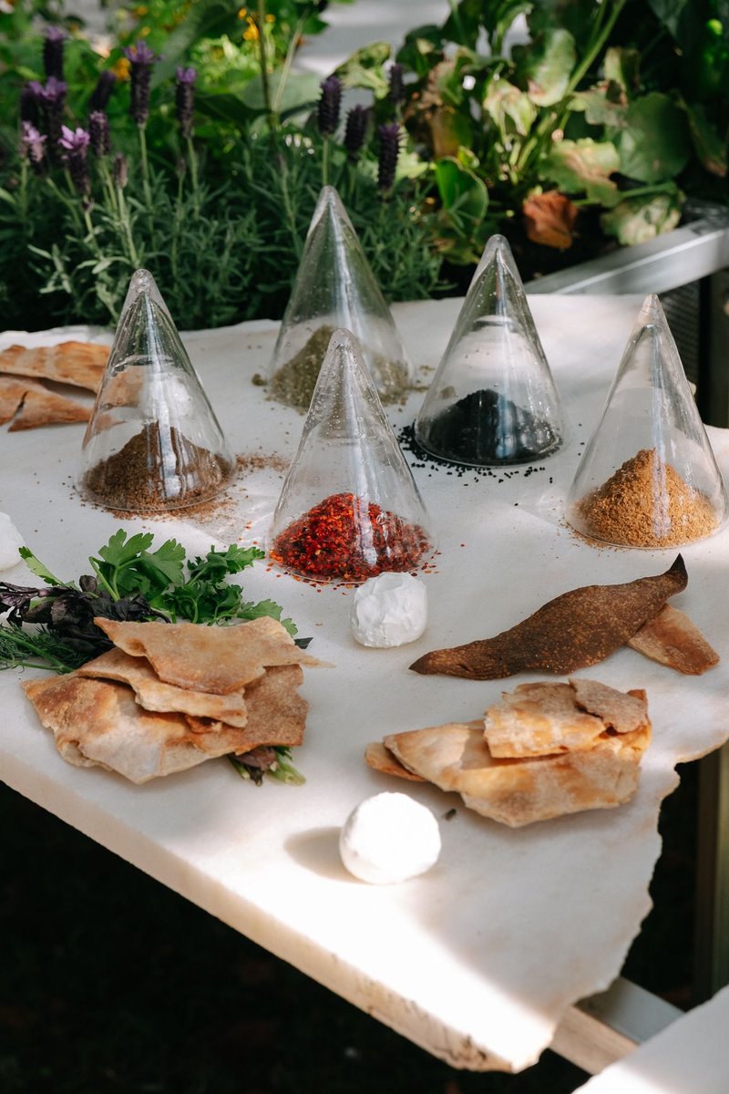 Tabletop display of glass pyramid vessels filled with colored spices and dried herbs