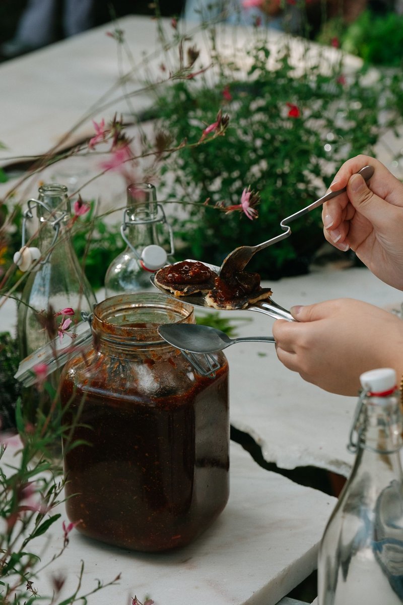 Hand holding a fork over a glass jar of preserve with wildflowers in the background