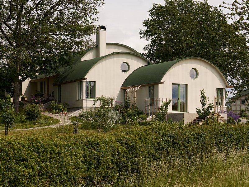 Garden elevation showing the three vaulted volumes with planted beds and a timber pergola in afternoon light