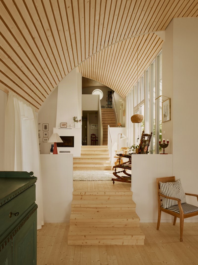 Interior hallway with timber slat vaulted ceiling, light wood flooring, and staircase ascending between white walls