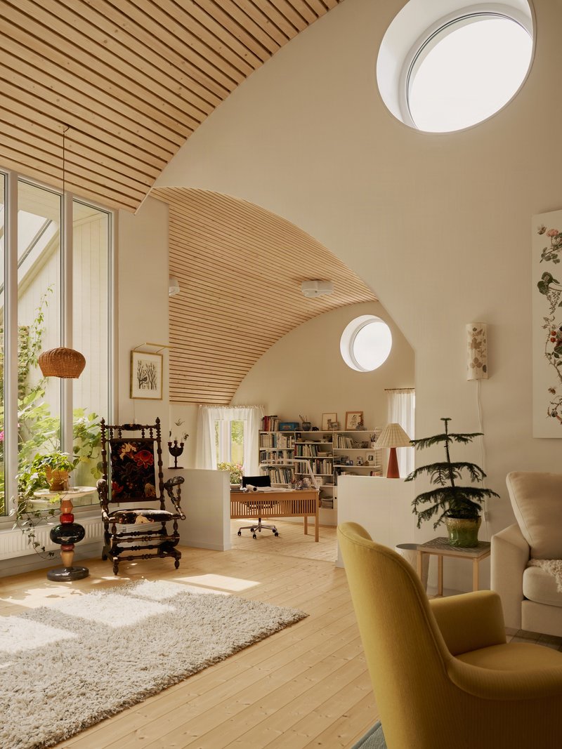 Living space with arched timber slat ceiling, circular skylights, and sunlight filtering through tall windows
