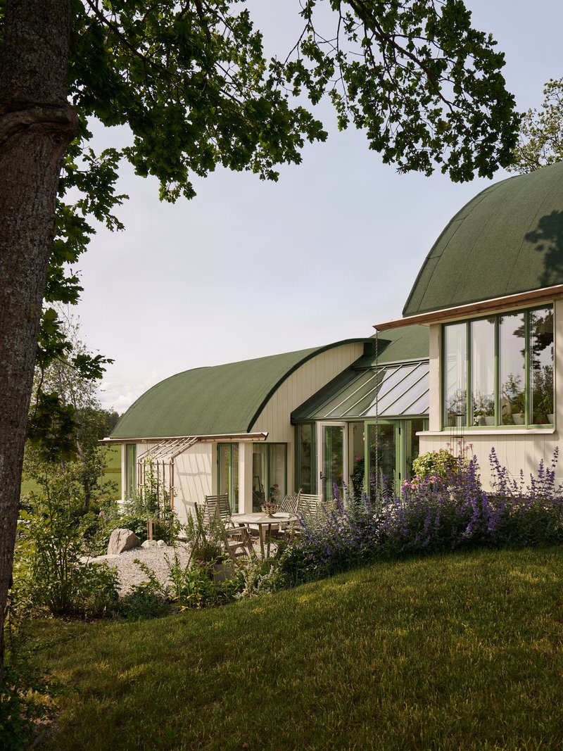 Corner terrace with glazed walls beneath the overhanging green barrel roof and oak tree canopy overhead