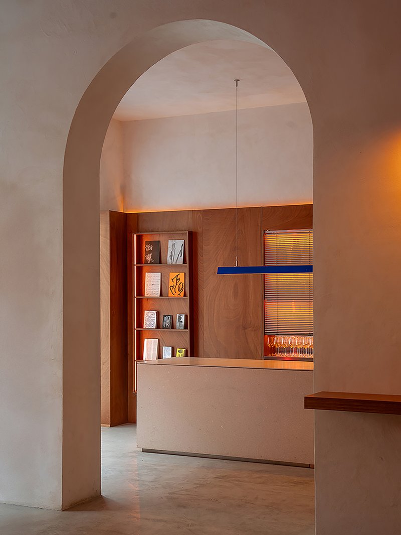 View through arched opening to timber service counter with built-in shelving and warm recessed lighting