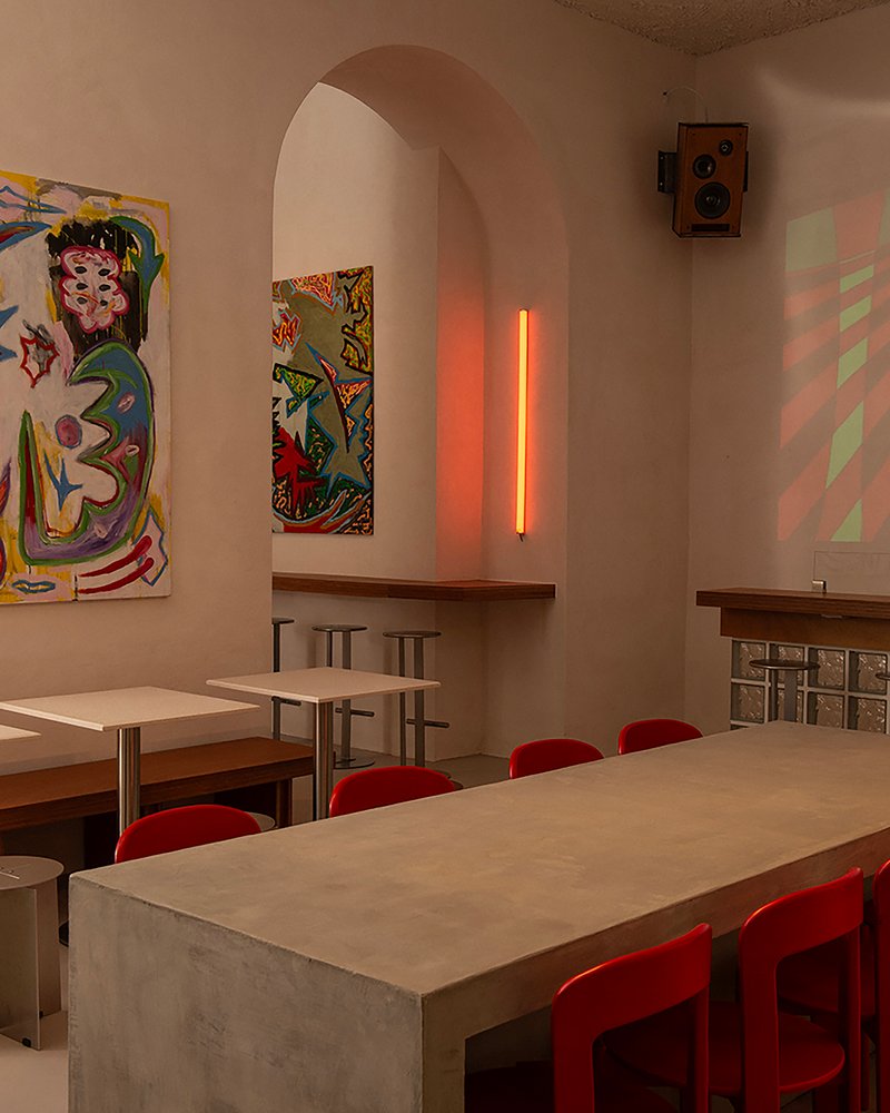 Dining table with red chairs beneath arched alcove with orange tube light and colorful paintings
