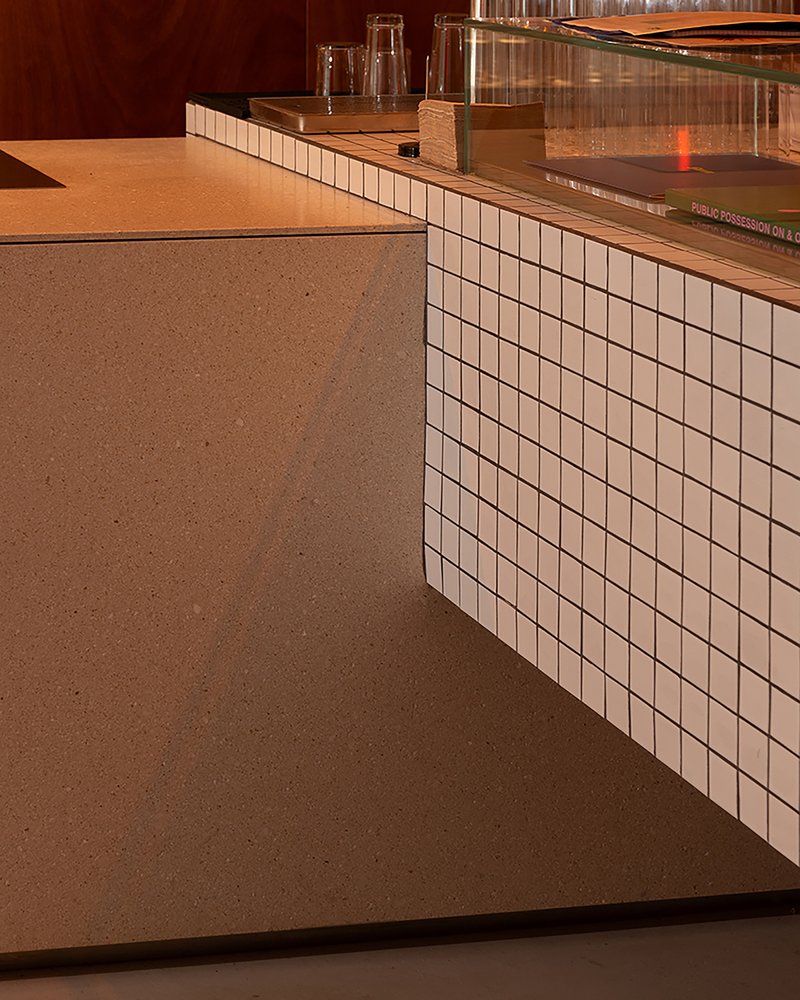 Bar counter clad in white square tiles with terrazzo flooring and warm overhead lighting