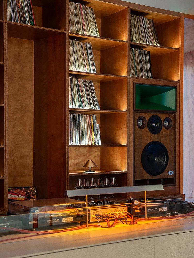 Timber shelving unit holding vinyl records with integrated speakers and audio equipment under yellow lighting