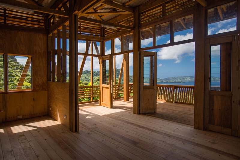 Interior room with exposed timber framing opening onto a railed deck overlooking distant mountains and water