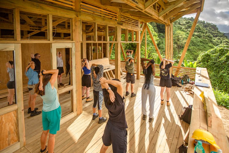 Construction workshop in progress with participants assembling timber frame elements on the plywood floor