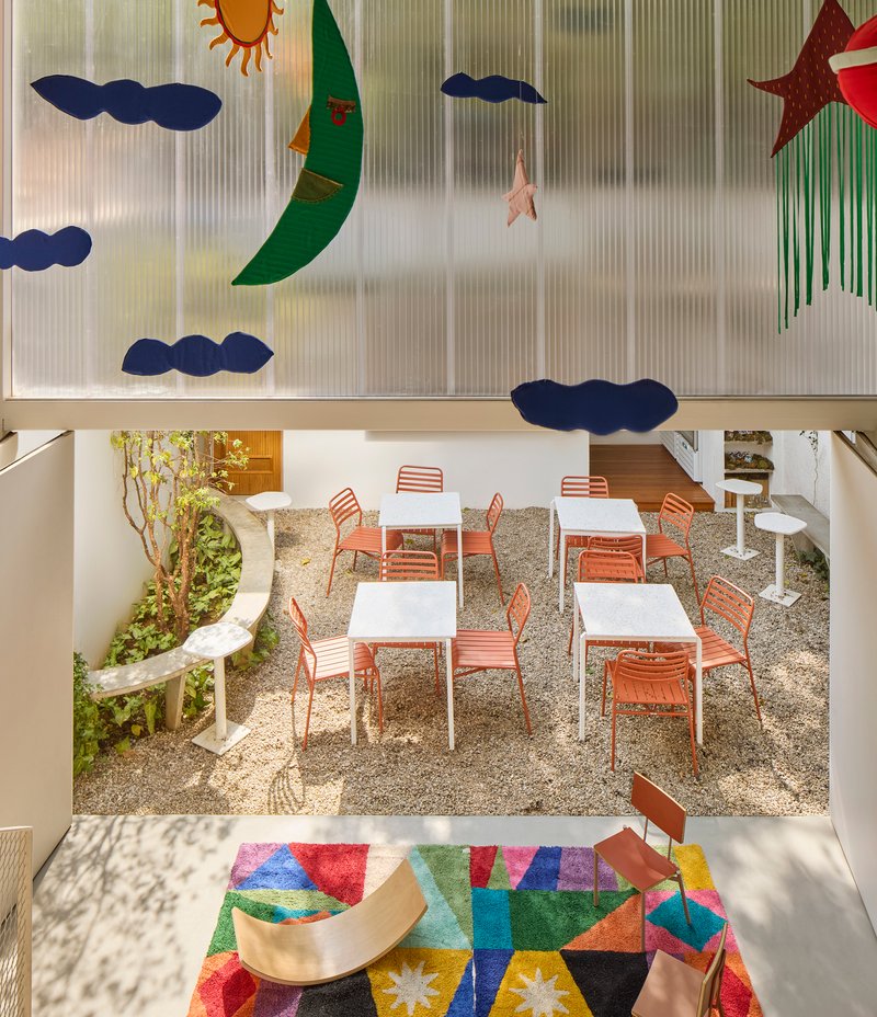 Double-height view through translucent wall with celestial appliques into gravel courtyard with orange chairs