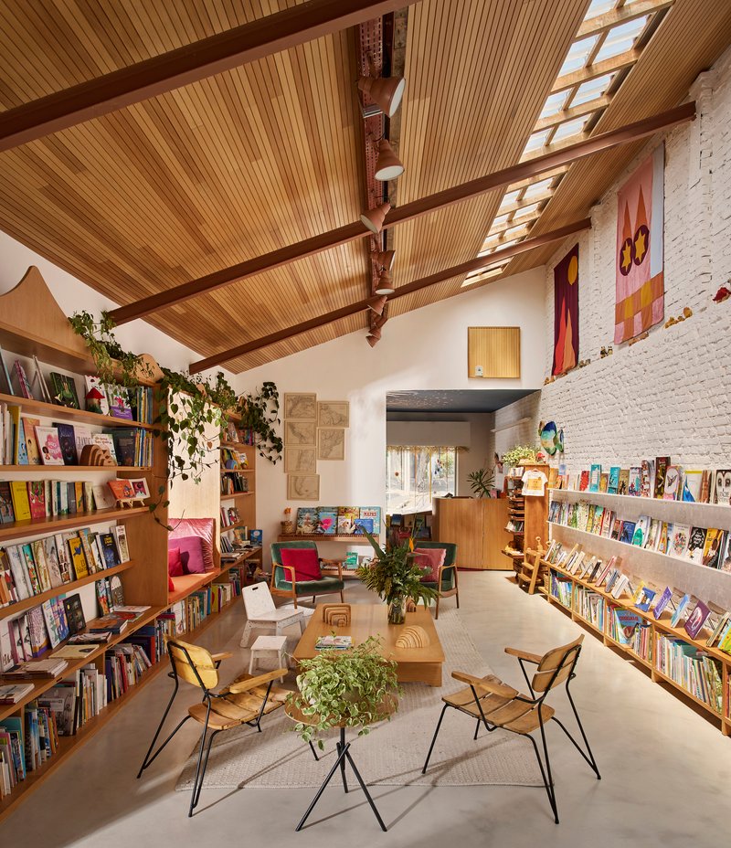 Interior of a bookshop with timber-slatted ceiling, exposed beams, skylights and trailing vines