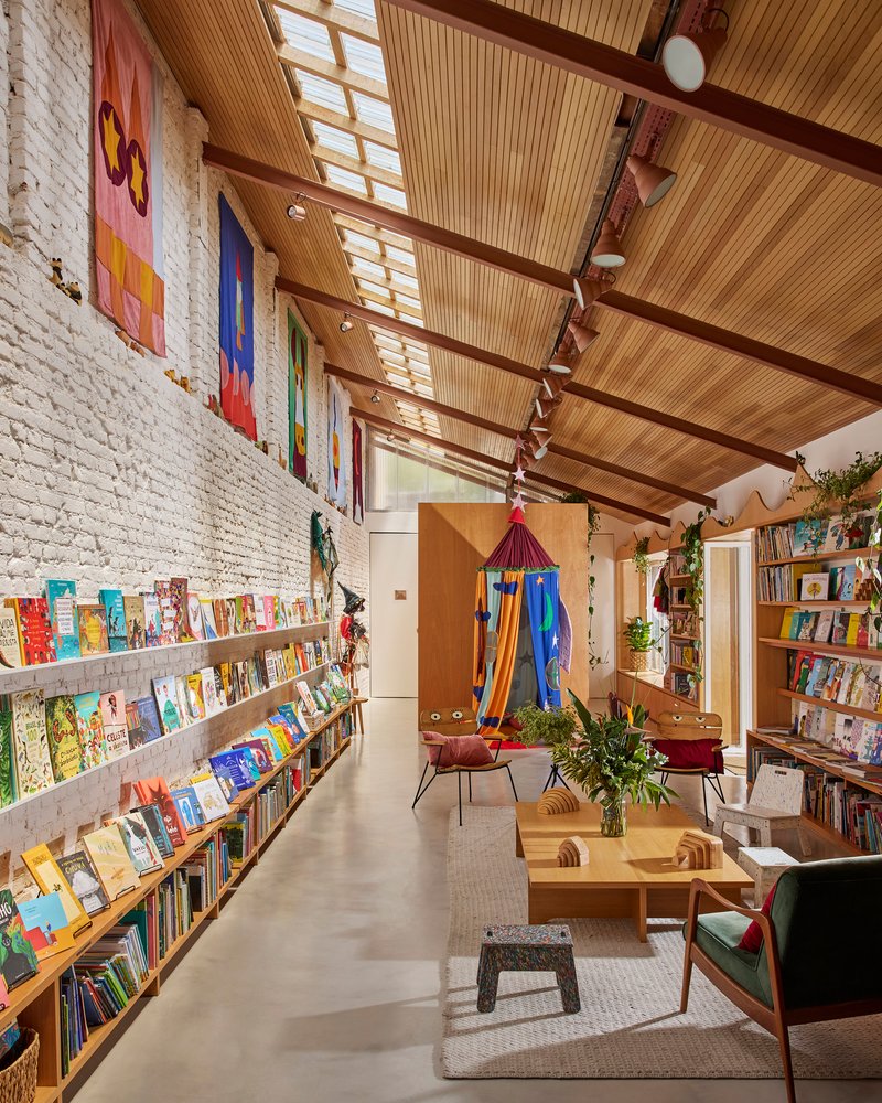 Long view through the bookshop showing timber ceiling, painted brick wall and central reading area