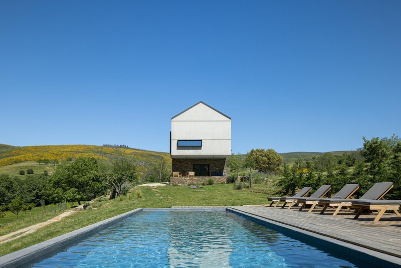 White rendered volume elevated on stone base beside swimming pool with timber deck and loungers