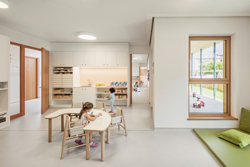 White classroom with timber-framed storage units and children at low tables under a ribbed ceiling