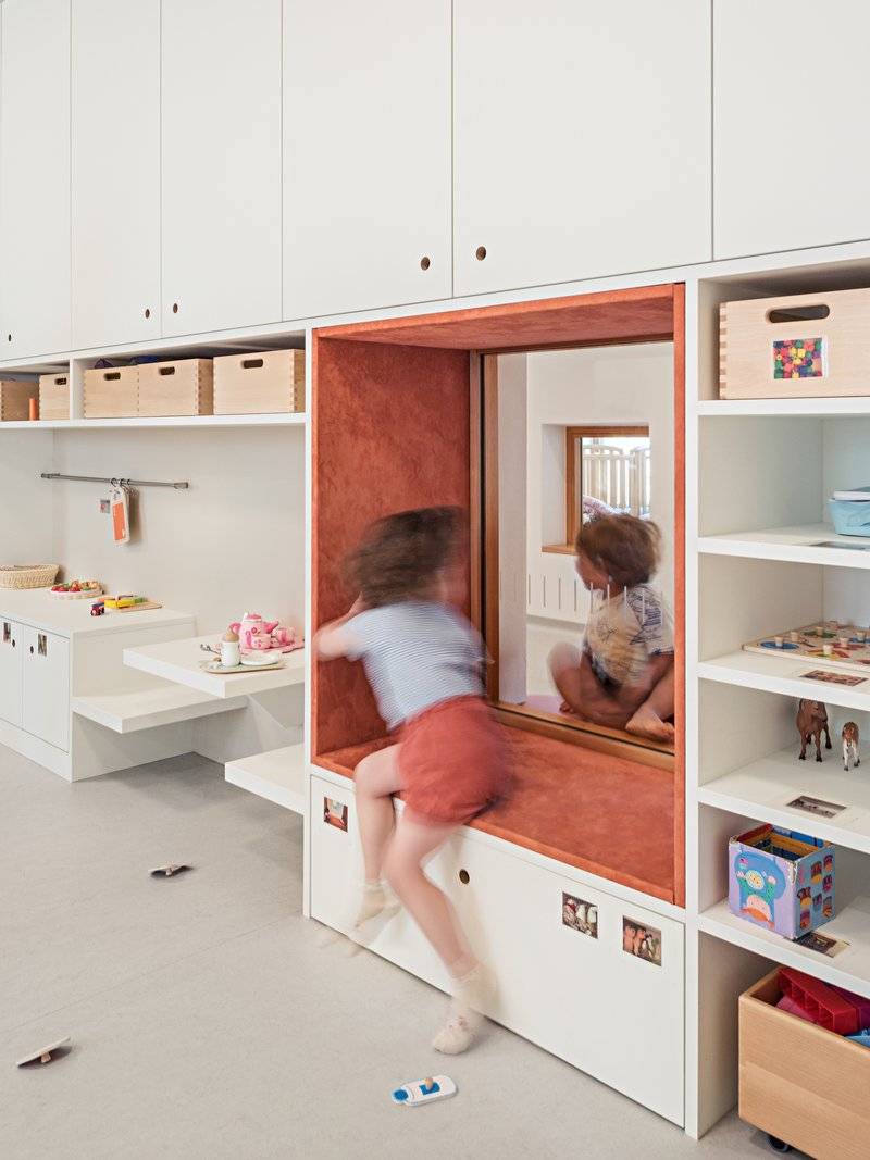 Built-in storage niche with orange plywood interior and children climbing through the opening