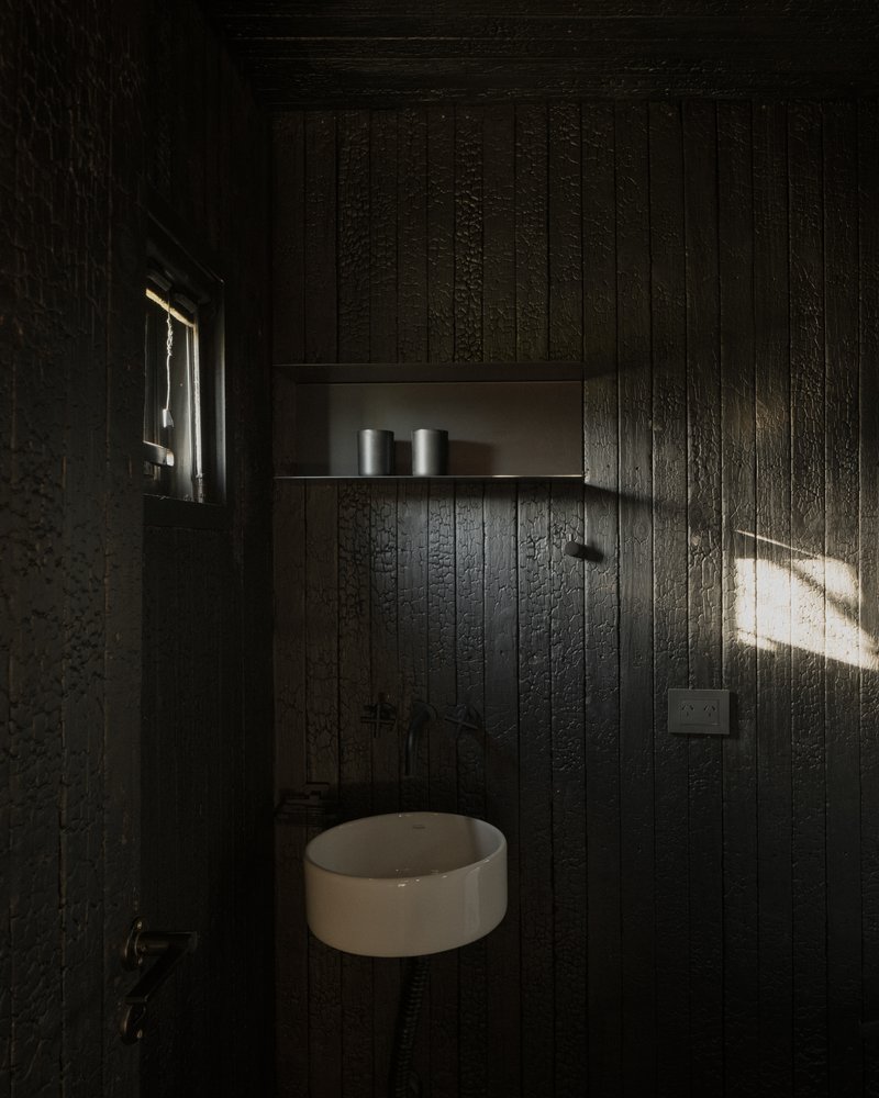 Small powder room with charred timber wall cladding and a round basin under a narrow shelf