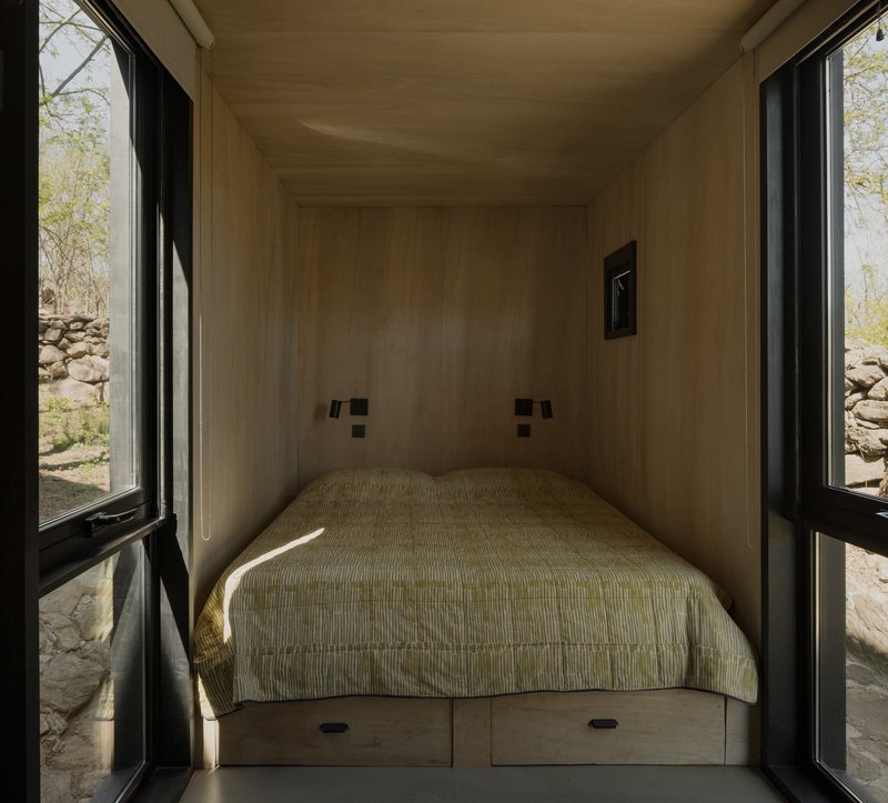 Built-in bed alcove with plywood lining and flanking black-framed glazed doors opening to a stone wall